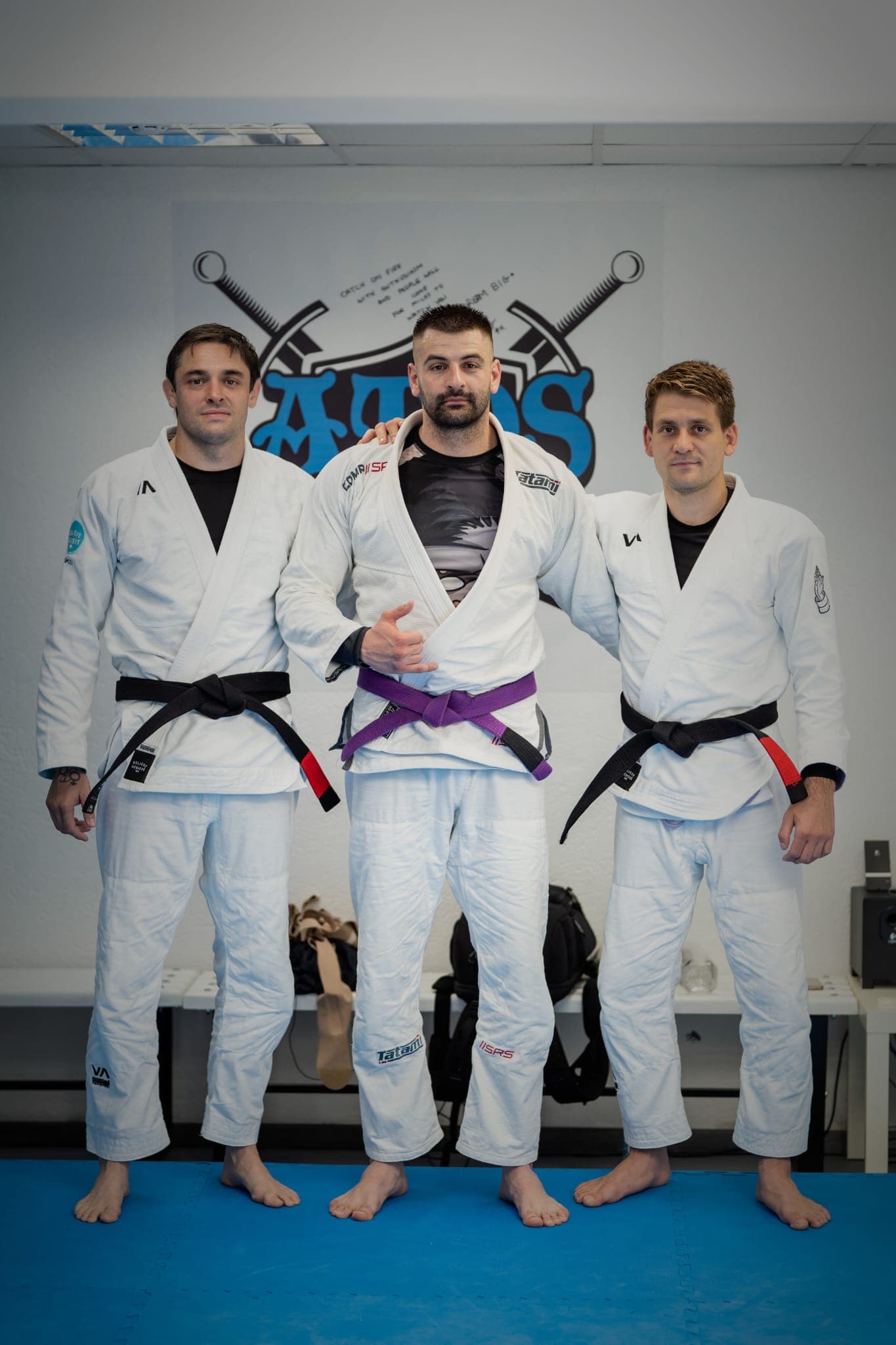Trei sportivi în kimono alb, cu centuri neagră și violet