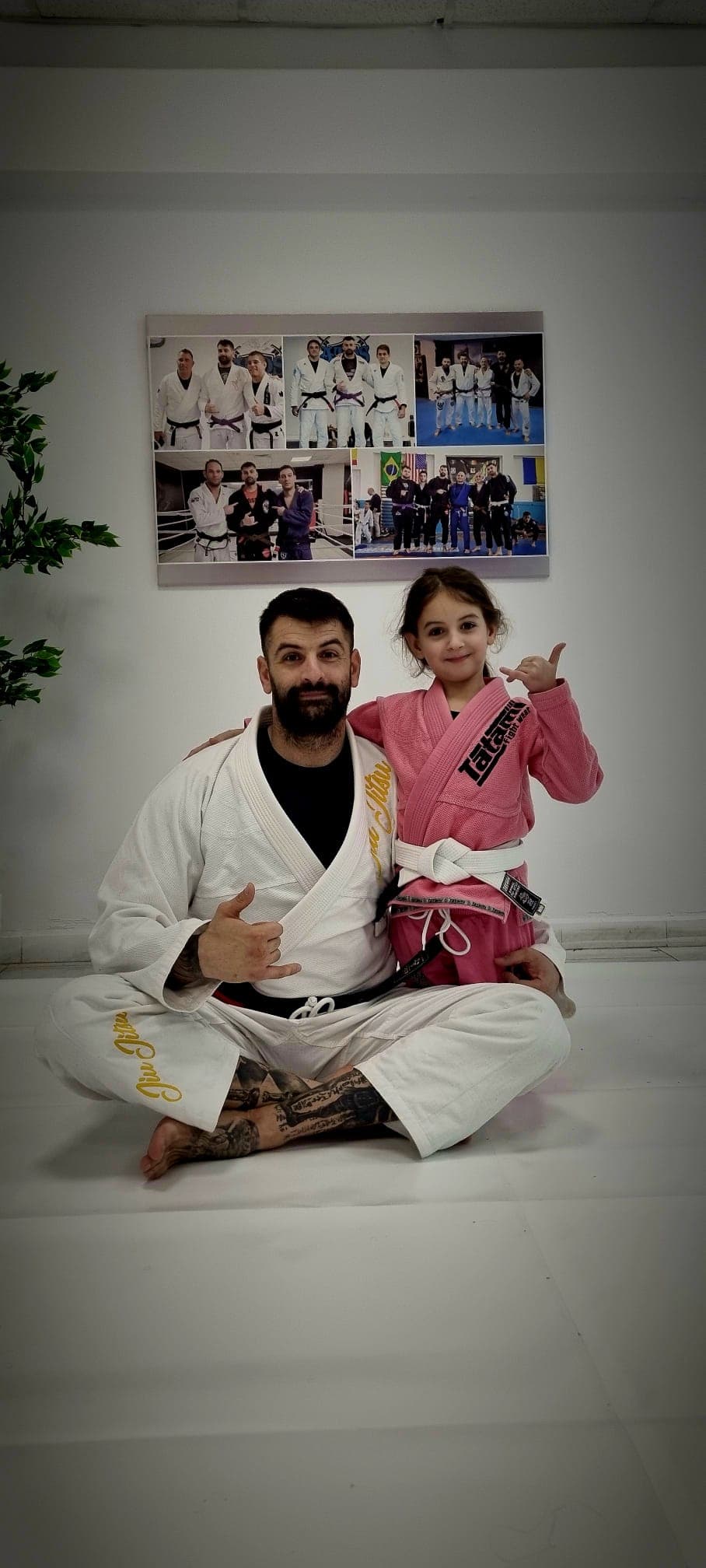 Un antrenor în kimono alb, așezat pe saltea lângă o fetiță în kimono