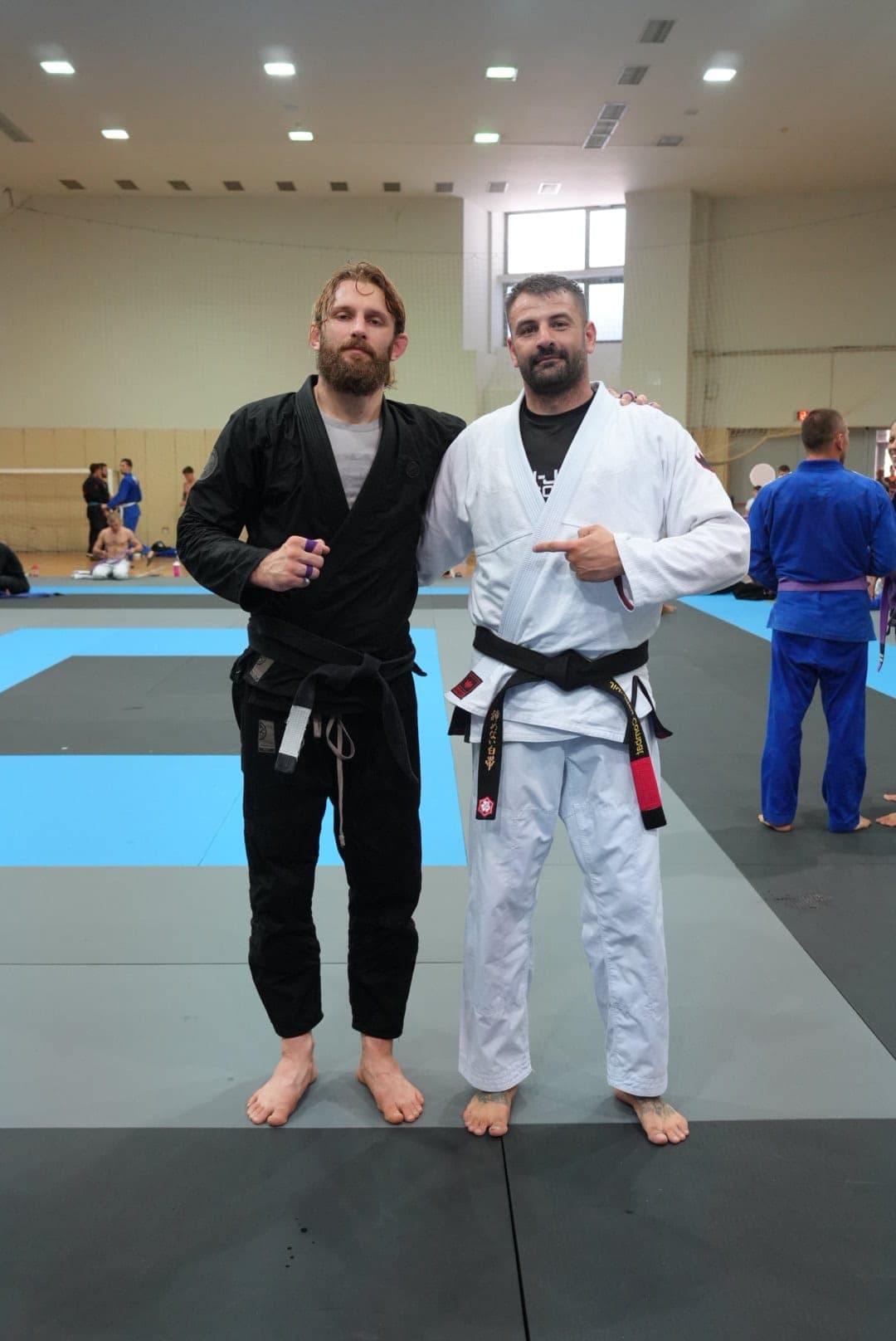 Doi sportivi pe salteaua de concurs, unul în kimono negru, celălalt în alb cu centură neagră