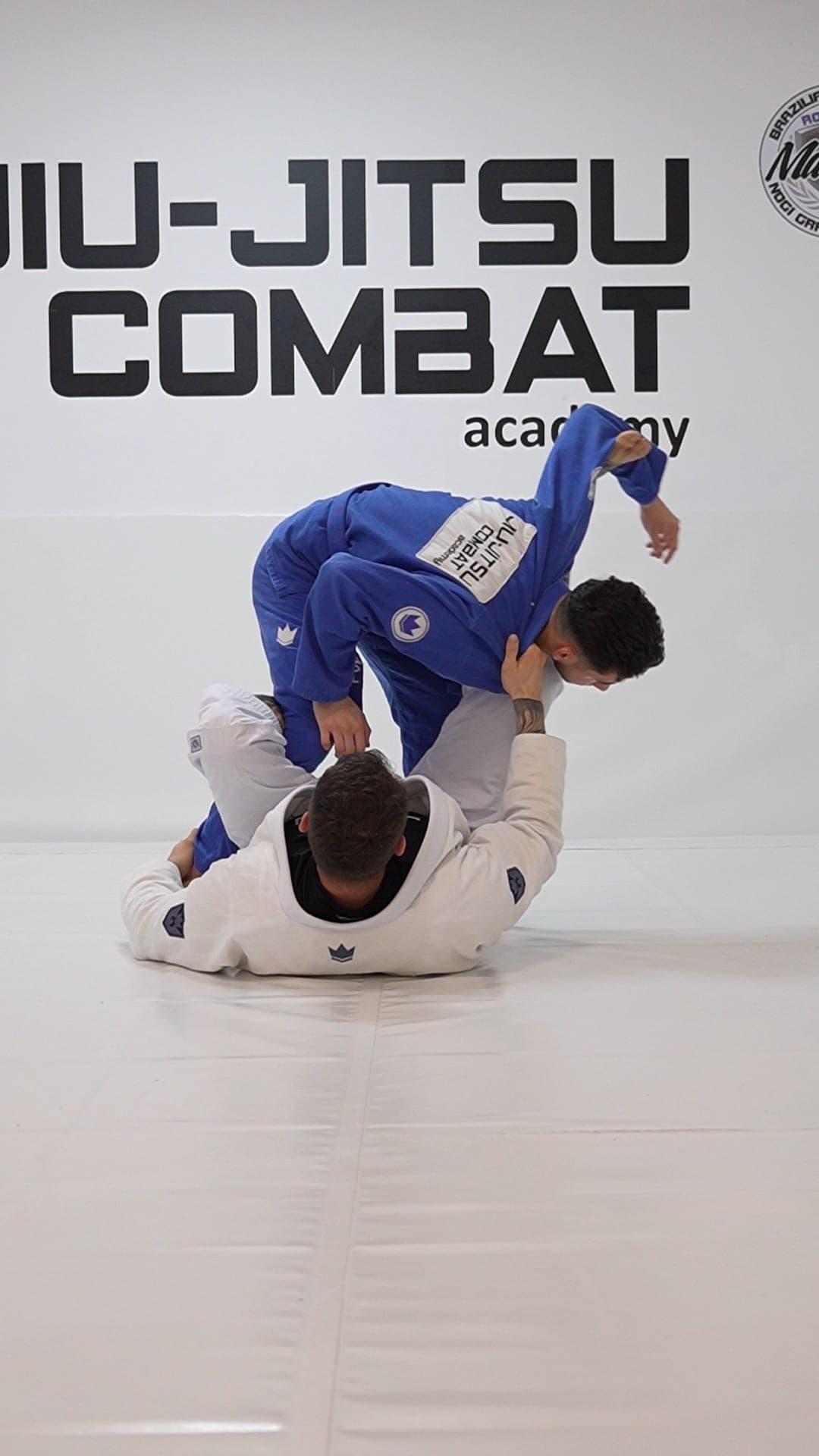 Demonstrație de tehnică: un sportiv în kimono albastru controlează adversarul la sol